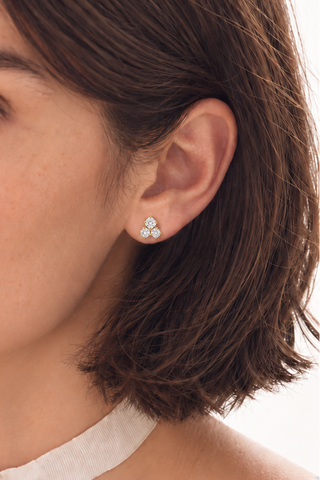 Close-up of a woman wearing a white choker necklace with a gold-toned pendant and a matching small stud earring against a clean white background.