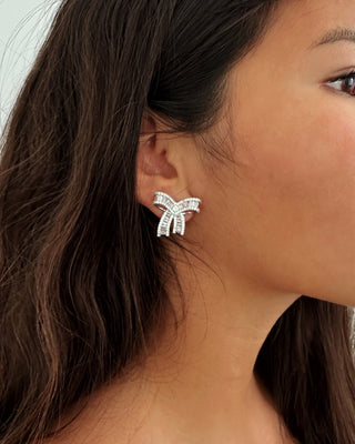 Close-up of a woman wearing a bow-shaped earring with a neutral background