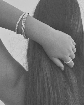 Person with long hair and hand holding it, wearing bracelets and rings.